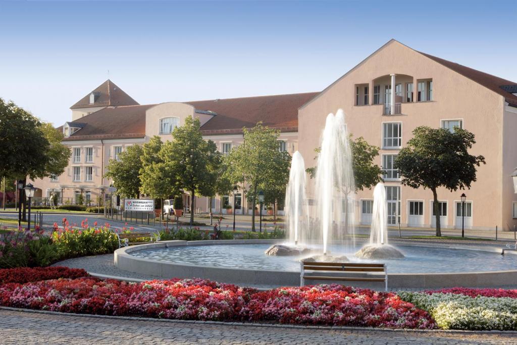 a fountain in front of a building with flowers at Hotel Maximilian in Bad Griesbach