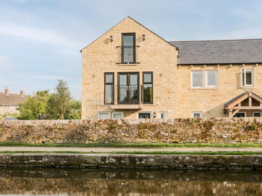 a brick house with a stone wall next to a river at 6 Lock View in Skipton