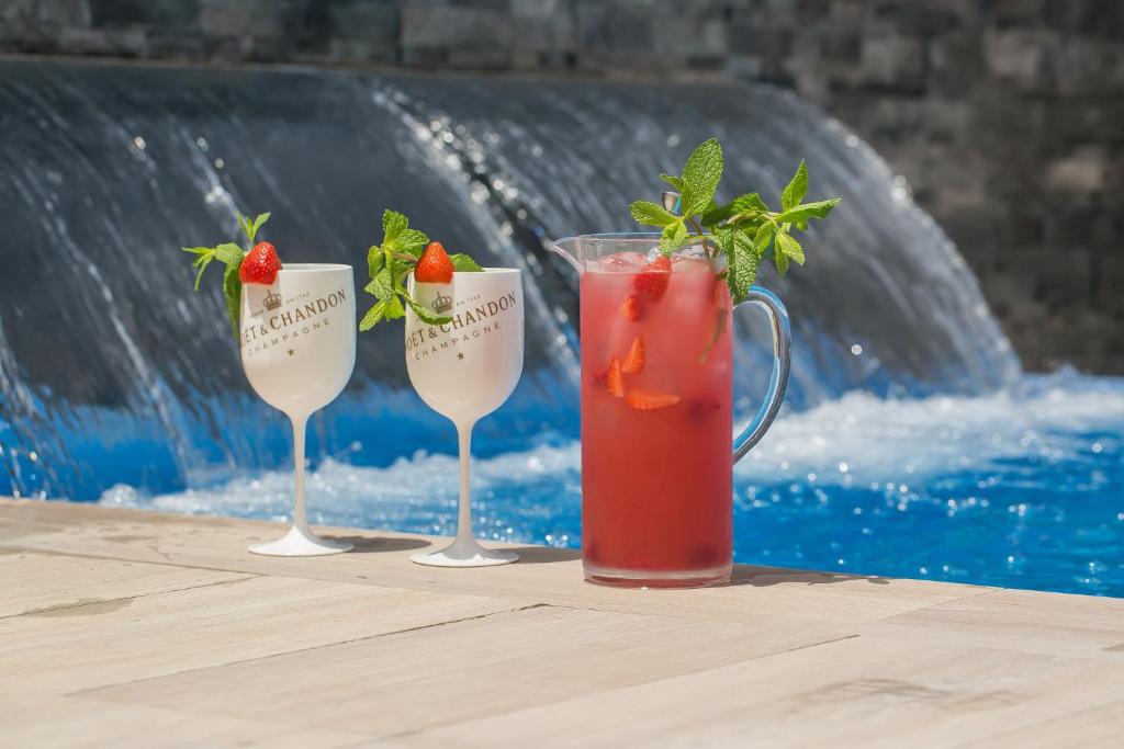 three wine glasses with strawberries and a drink next to a pool at Hotel Brö-Adults Recommended in Málaga