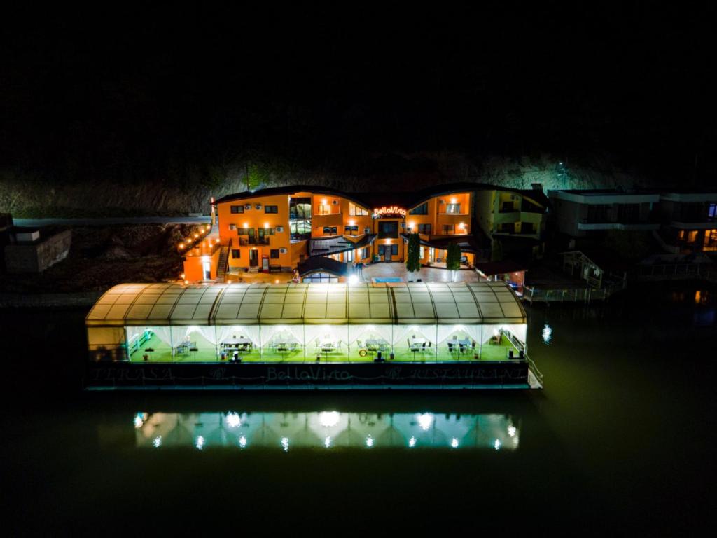 ein großes Gebäude mit nachts Licht auf dem Wasser in der Unterkunft Pensiunea Bellavista in Dubova