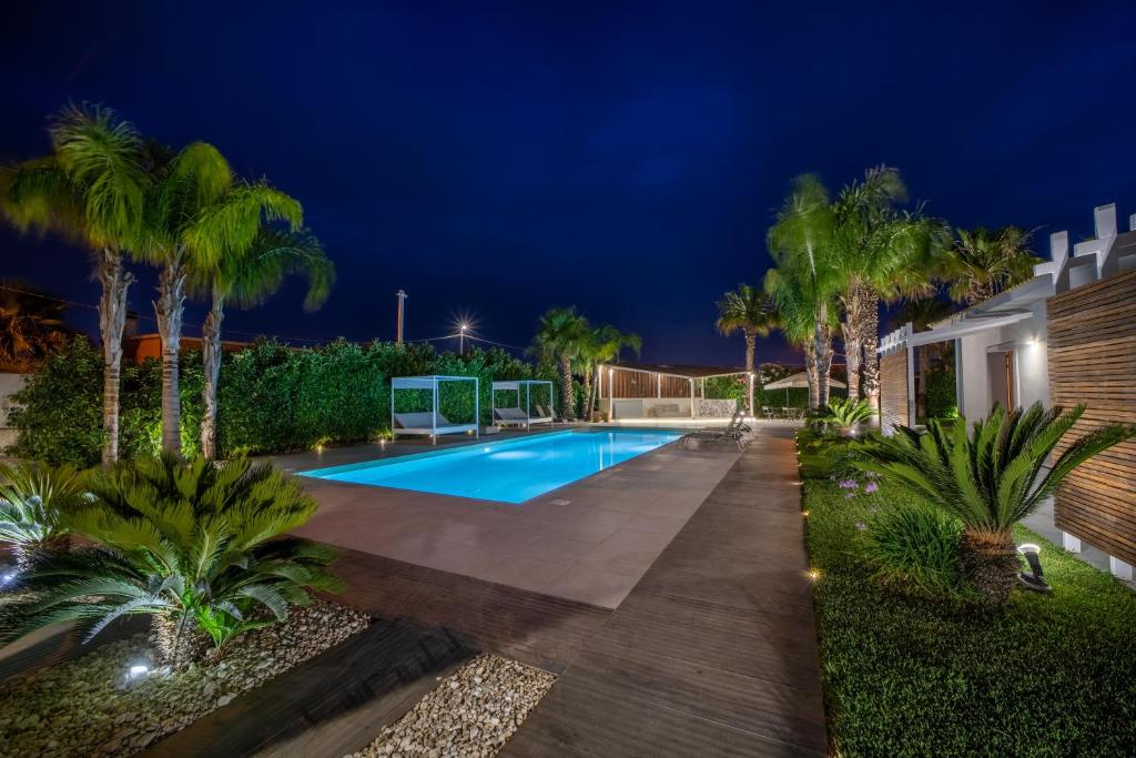 einen Pool in einem Garten mit Palmen in der Unterkunft Aqua Venere Pool & Suites in Marsala