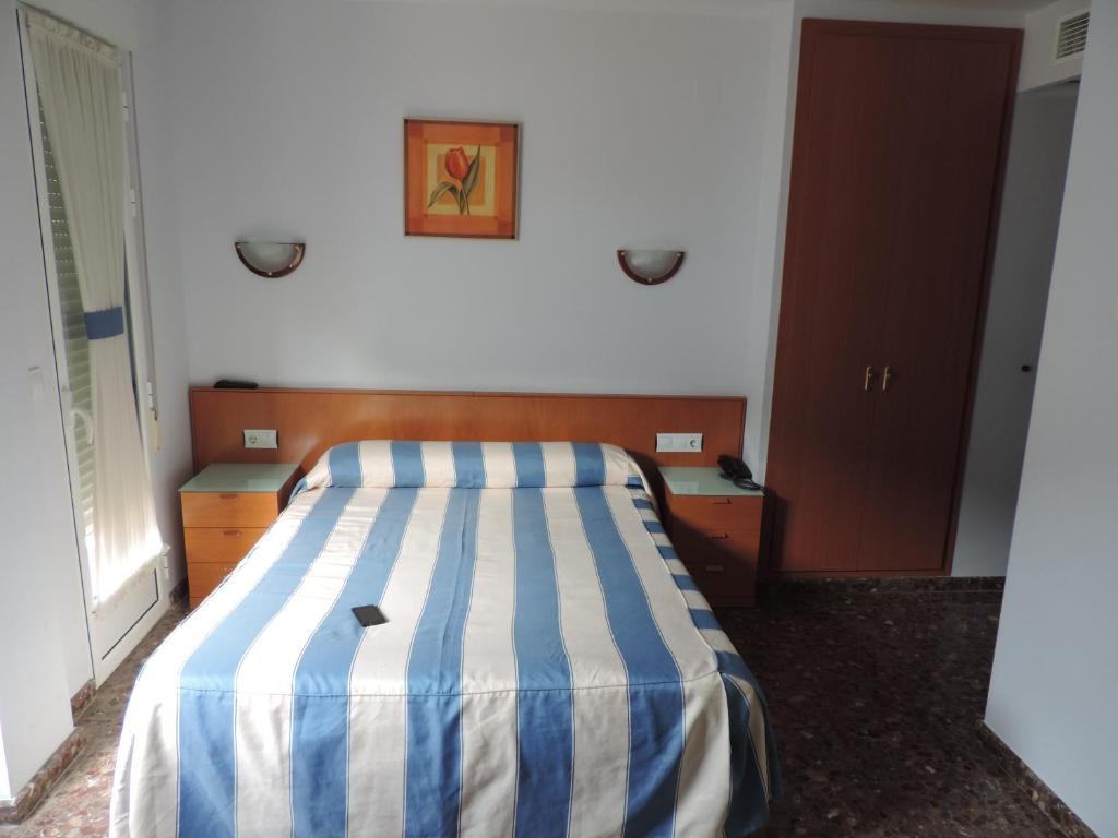 a bedroom with a bed with a blue and white striped blanket at Hotel Costa San Antonio in Cullera