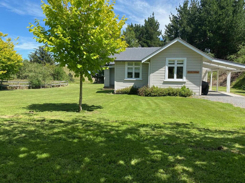 a small white house with a tree in the yard at Paratu Farm Cottage in a quiet rural setting. in  Waipukurau