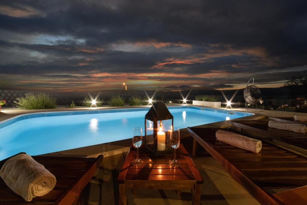 uma piscina à noite com uma mesa com copos de vinho e uma lanterna em Villa Ante em Marina
