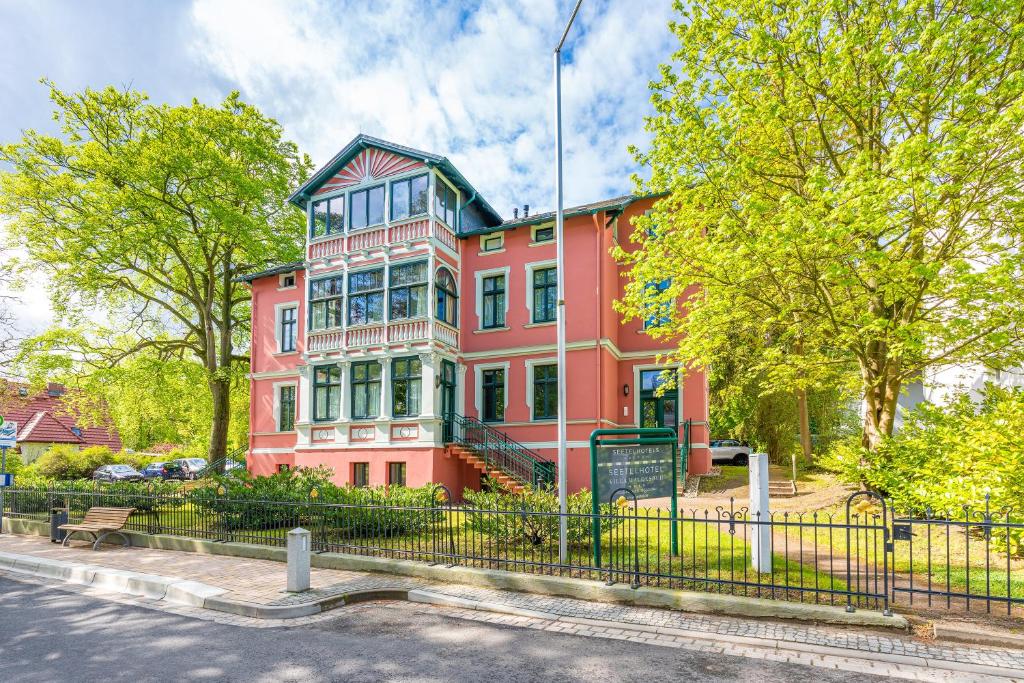 a large pink building with a fence in front of it at SEETELHOTEL Villa Waldesruh in Heringsdorf