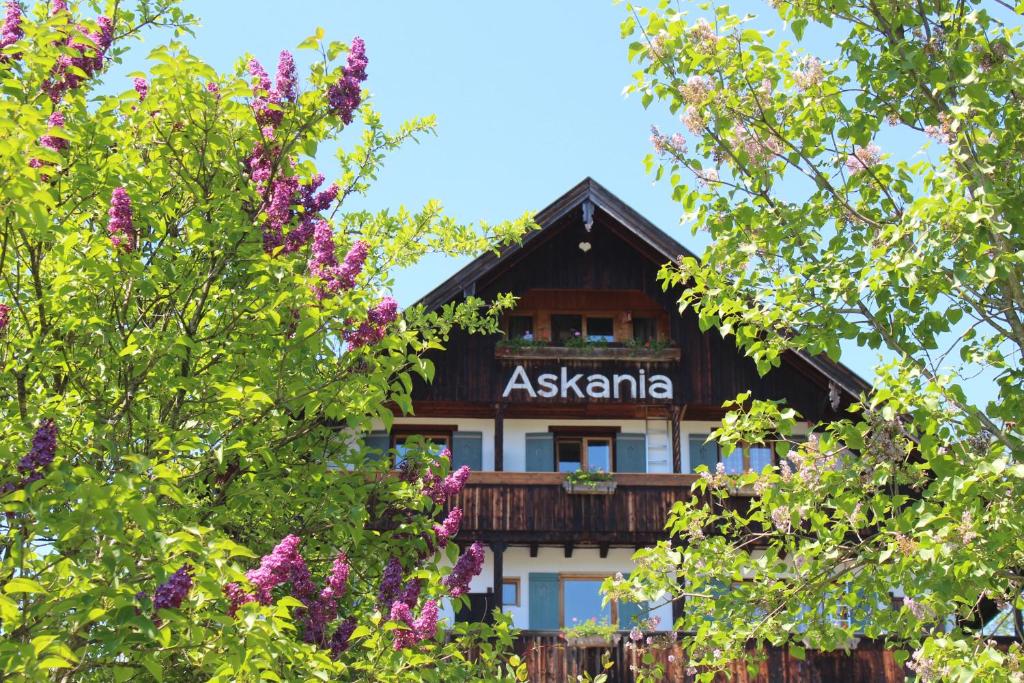 ein Gebäude hinter einigen Bäumen und lila Blumen in der Unterkunft Hotel Askania 1927 in Bad Wiessee