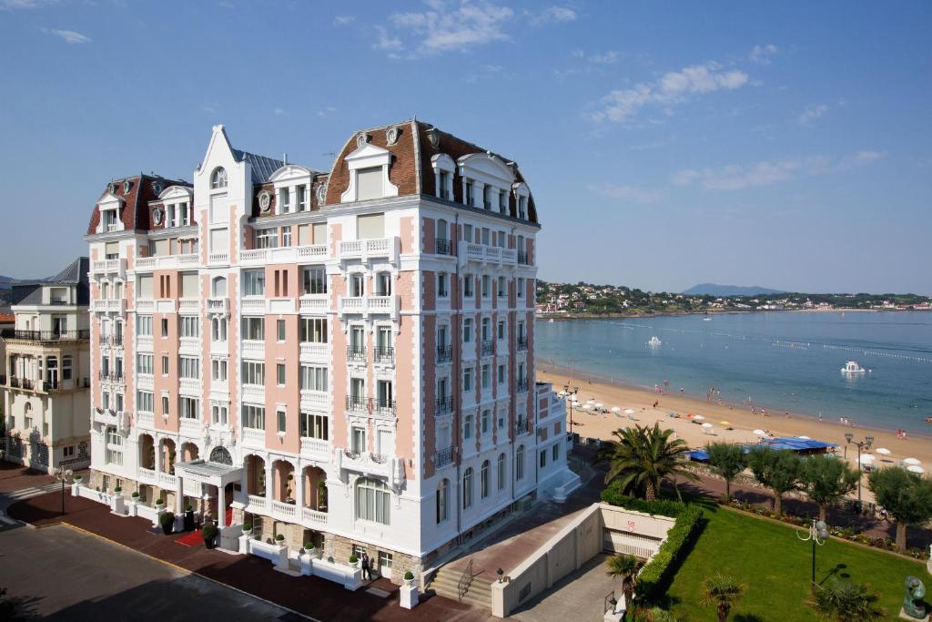 een groot wit gebouw met een strand op de achtergrond bij Grand Hôtel Thalasso & Spa in Saint-Jean-de-Luz