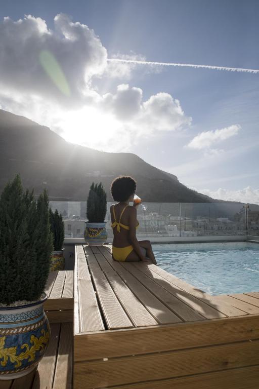 a woman sitting on a bench next to a swimming pool at Luxmarì Hotel & Spa in Castellammare del Golfo