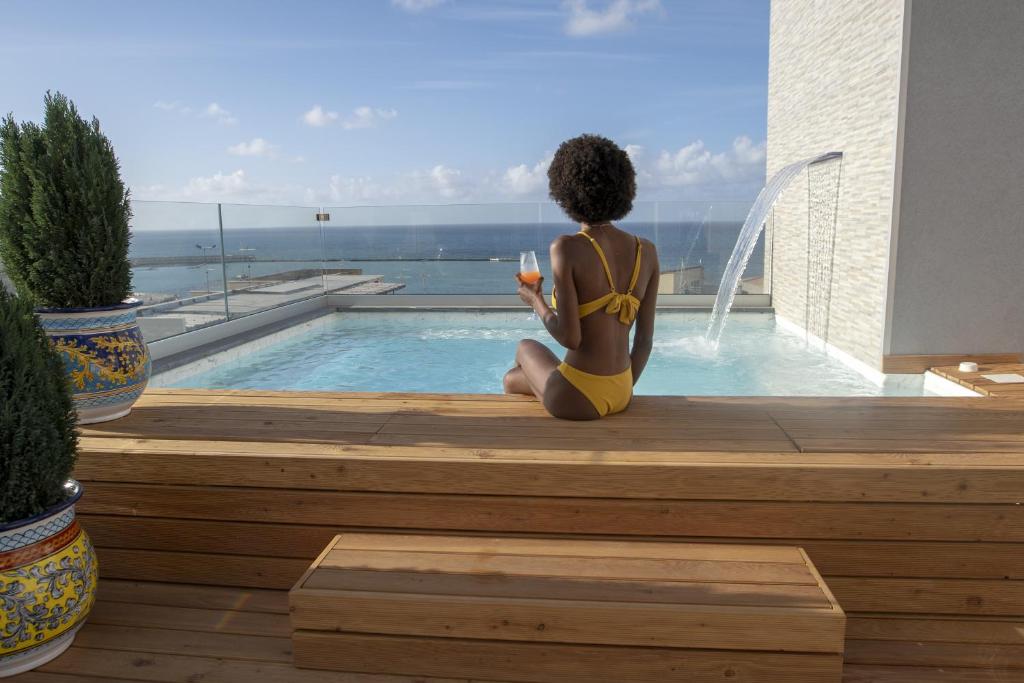 a woman in a yellow bikini sitting next to a swimming pool at Luxmarì Hotel & Spa in Castellammare del Golfo