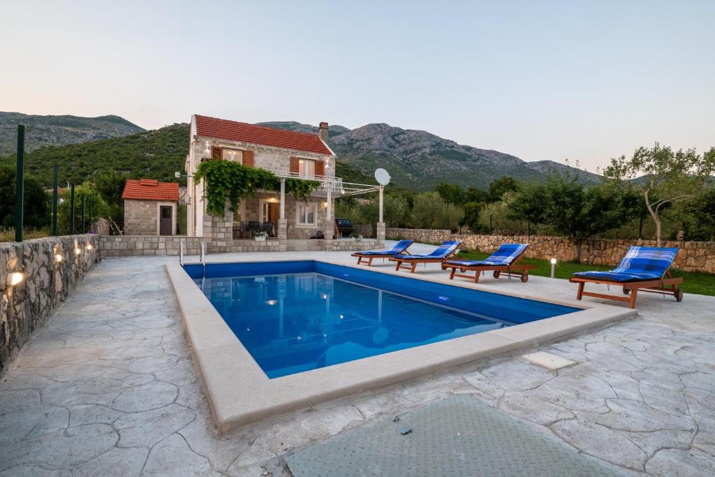 a swimming pool with two blue chairs and a house at Villa Rustica in Neum