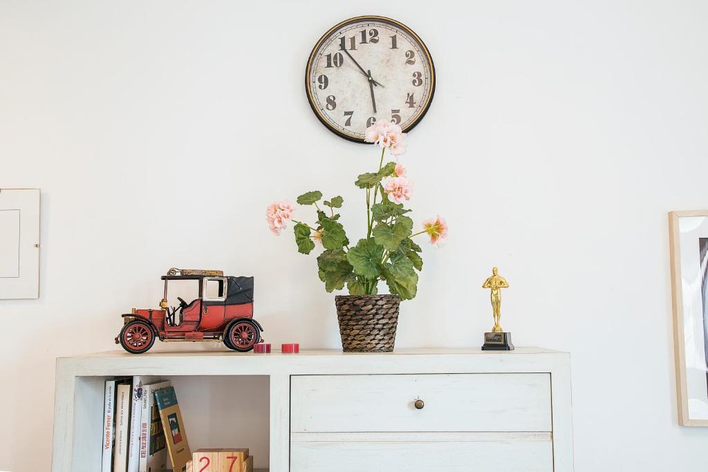 une horloge au-dessus d'une armoire blanche avec une plante dans l'établissement RentalSevilla De paseo por los Remedios, à Séville