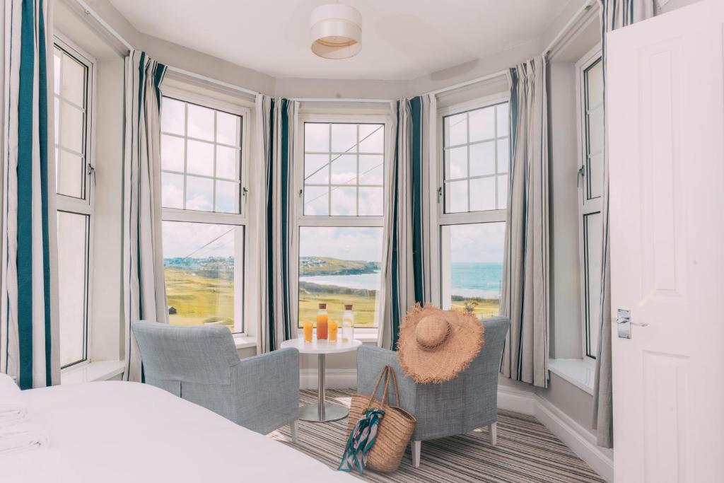 a bedroom with a bed and chairs and windows at Oceanside Lifestyle Hotel in Newquay