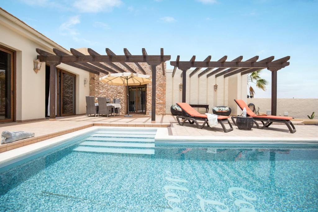 a swimming pool with two chairs and an umbrella at Casa Rural La Morisca in Tuineje