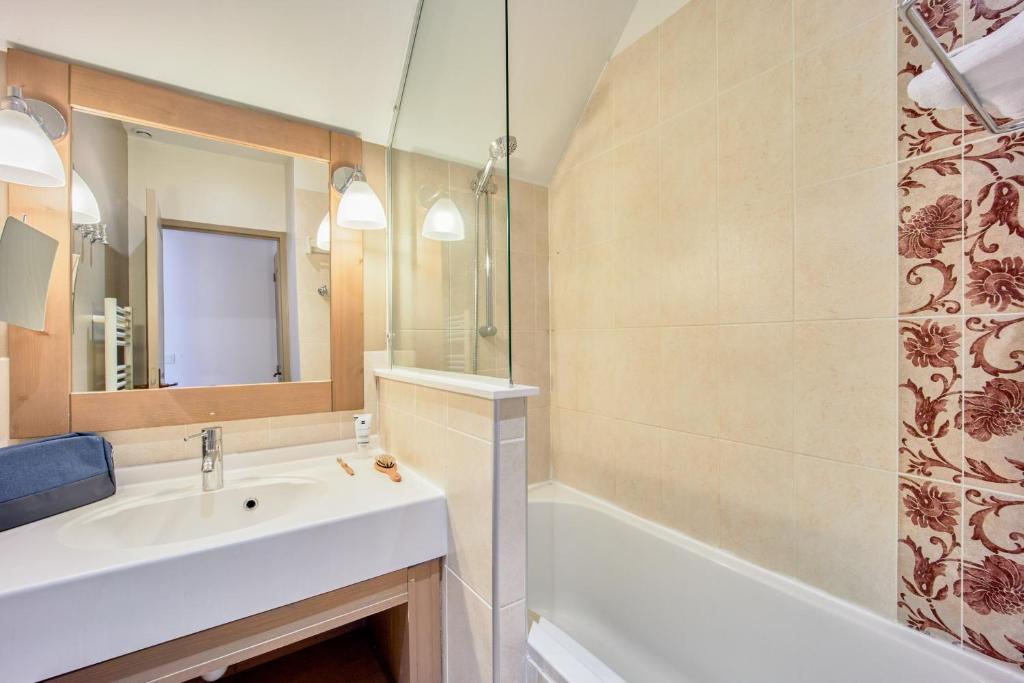 a bathroom with a sink and a tub and a mirror at Pierre & Vacances Premium Residence & Spa Houlgate in Houlgate