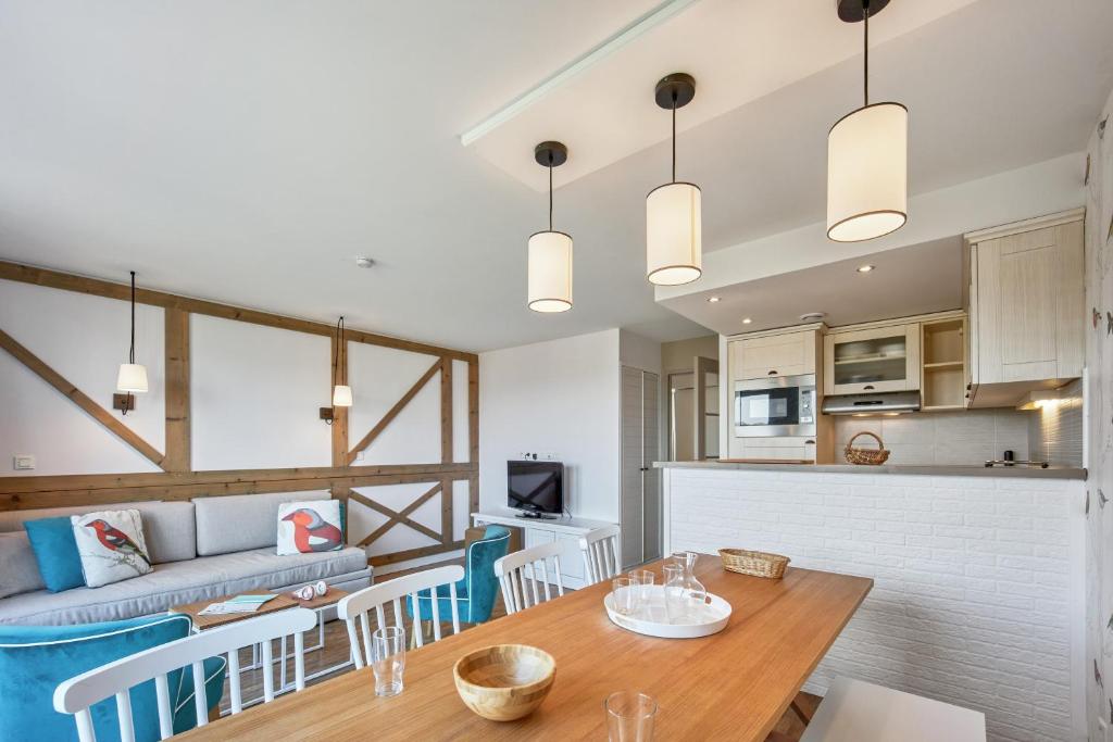 a kitchen and living room with a wooden table and chairs at Pierre & Vacances Premium Residence & Spa Houlgate in Houlgate