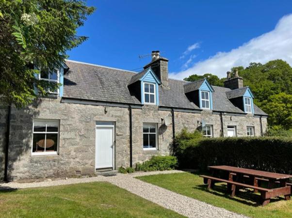 una casa in pietra con un tavolo da picnic di fronte di Burnside & Jocks Cottage on the Blarich Estate a Rogart