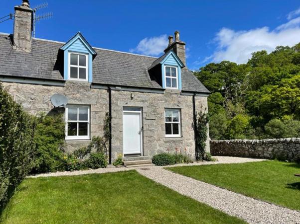 a large stone house with a grass yard at Burnside Cottage on the Blarich Estate in Rogart