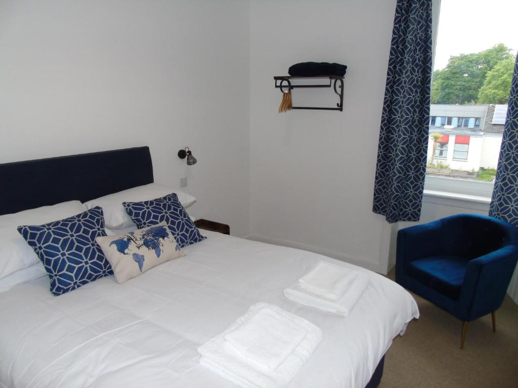um quarto com uma cama branca e uma cadeira azul em Snug - Sealladh Mara Apartment em Helensburgh