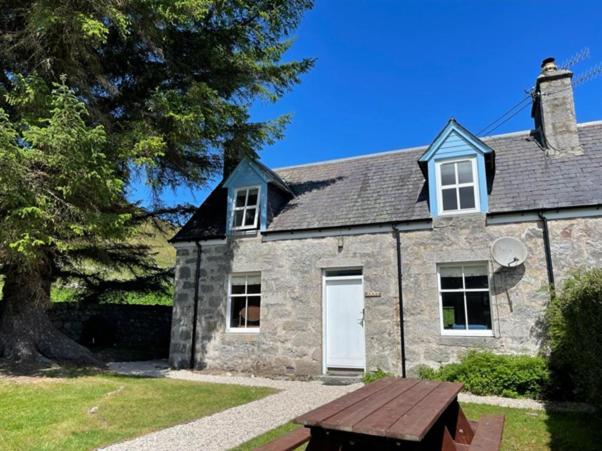 uma casa de pedra com um banco à frente em Jock's Cottage on the Blarich Estate em Rogart