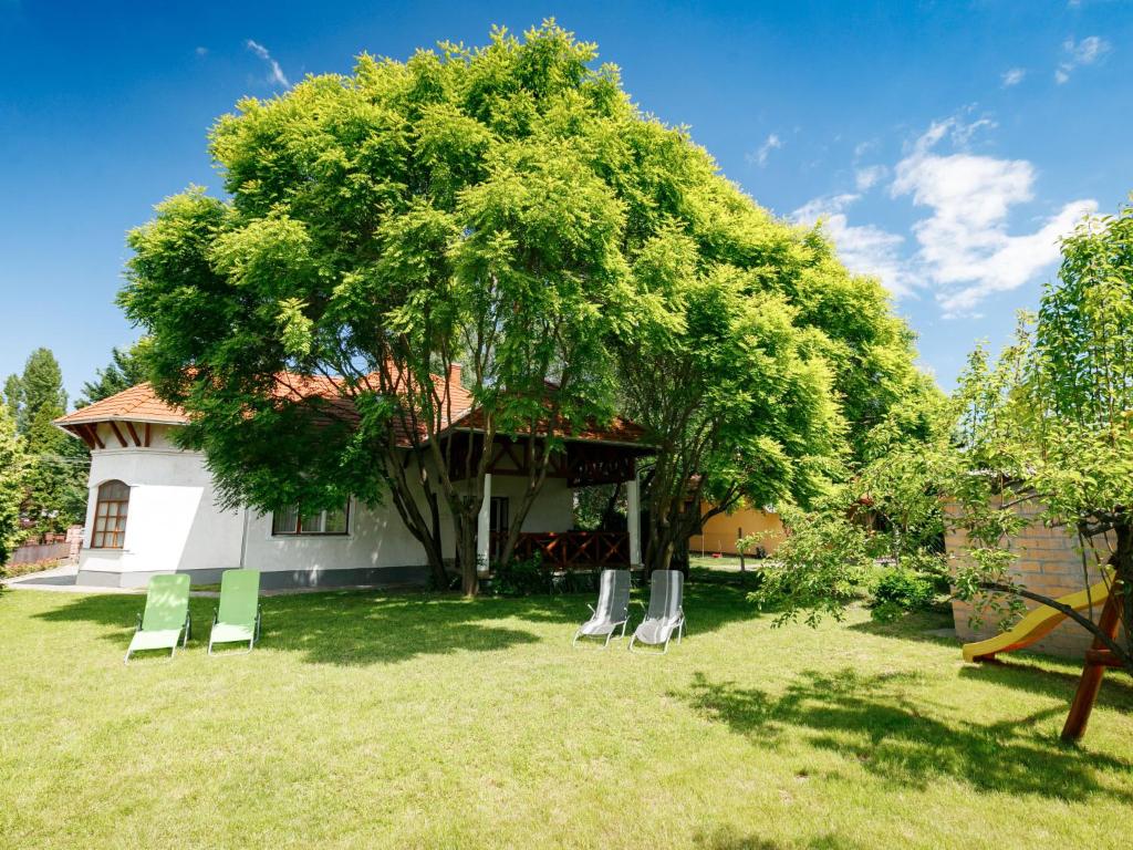a tree with white chairs in a yard at Holiday Home Marian by Interhome in Balatonboglár