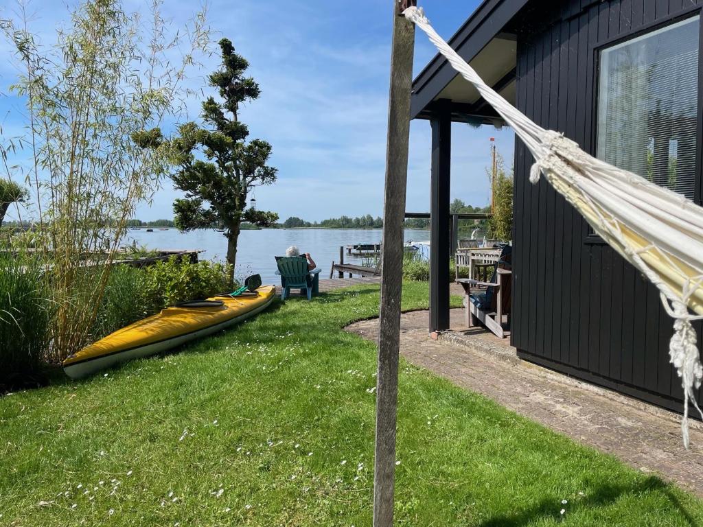 ReeuwijkにあるThe Outpost Lakehouse- enjoy our house at Reeuwijkse Plassen - near Goudaの芝生の上にボートを乗せた家の隣にあるハンモック