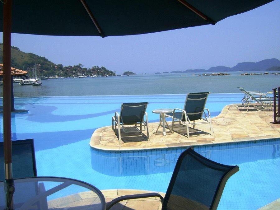 einen Pool mit Stühlen und einem Tisch und Wasser in der Unterkunft Angra dos Reis - Porto Bali - SUÍTE no Porto Bali Resort in Angra dos Reis