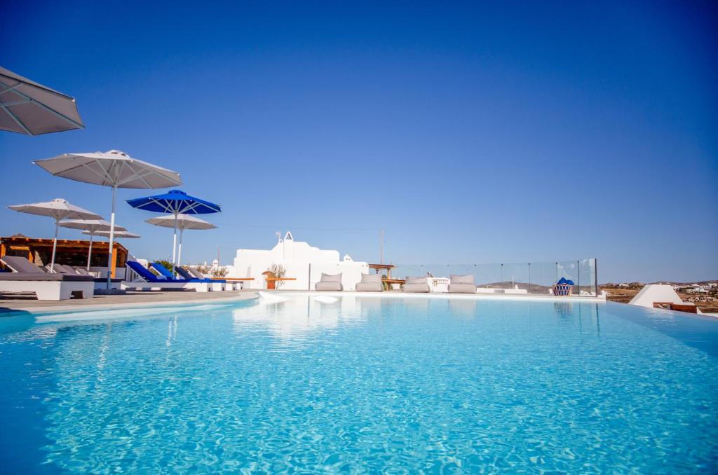 a pool with blue water and white buildings and umbrellas at Agnandi Cielo in Tourlos