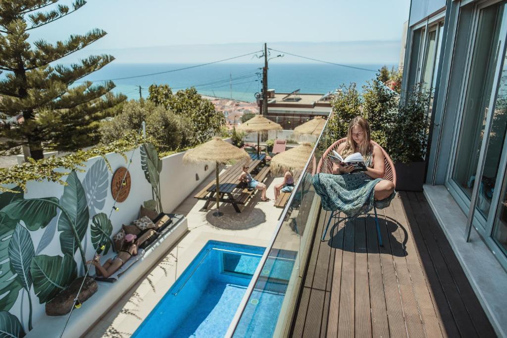 una mujer sentada en un balcón junto a una piscina en The Salty Pelican Yoga & Surf Retreat, en Ericeira