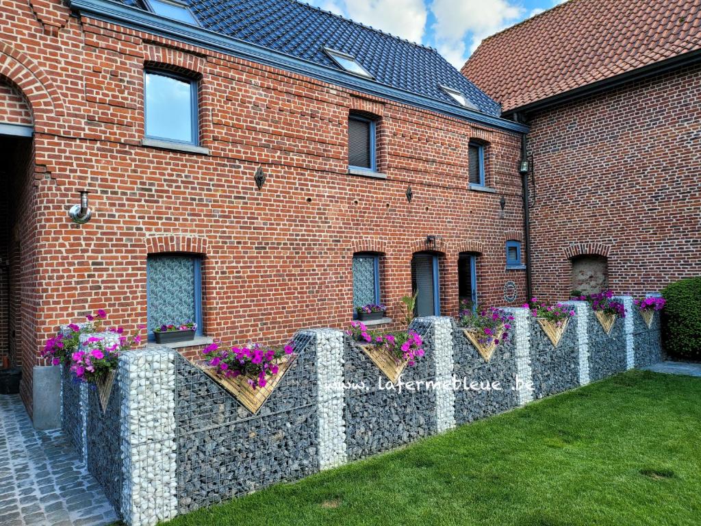 un bâtiment en briques avec des fleurs sur une clôture dans l'établissement La Ferme Bleue, à Tournai