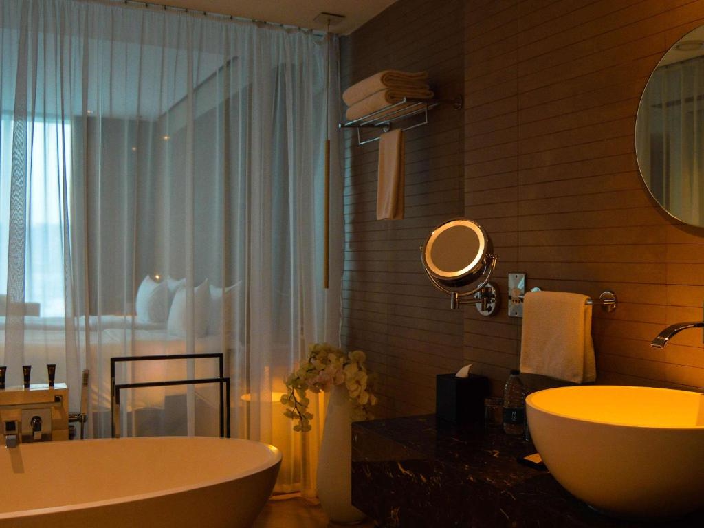 a bathroom with a tub and a sink and a mirror at The Canvas Dubai - MGallery Hotel Collection in Dubai