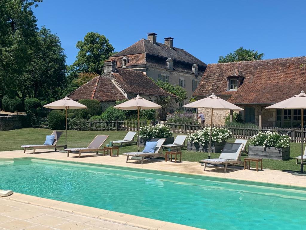 a pool with chairs and umbrellas in front of a house at Manoir de Malagorse in Cuzance