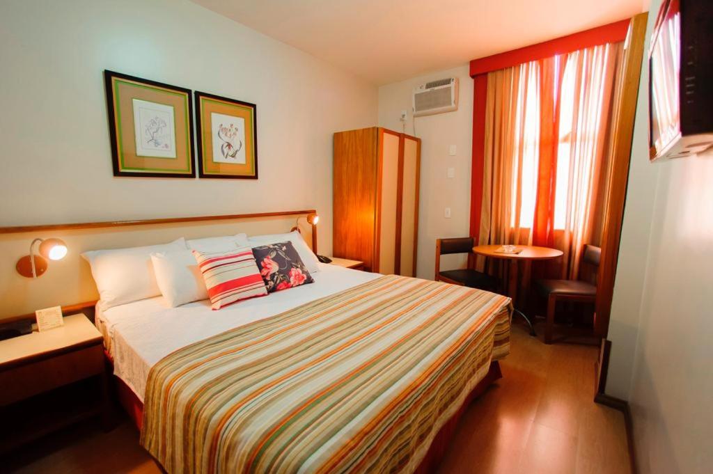 a hotel room with a bed and a desk and window at César Inn Juiz de Fora Hotel in Juiz de Fora