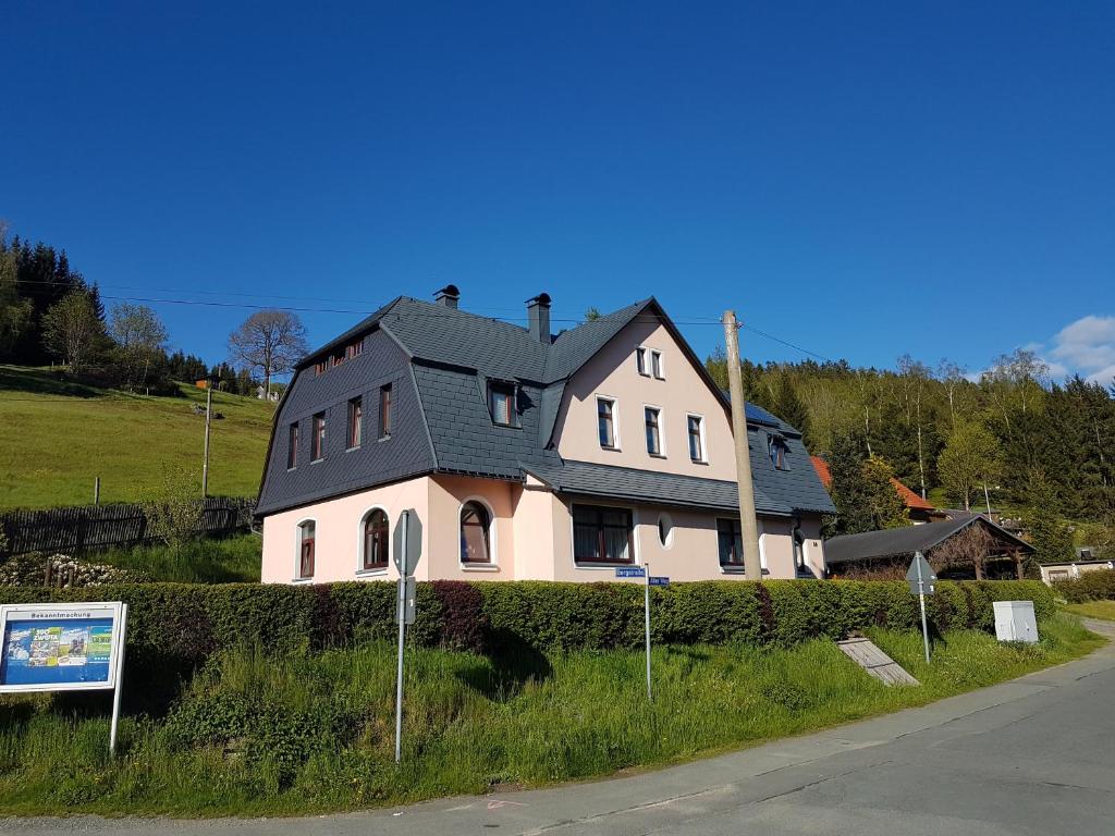 ein weißes Haus mit einem schwarzen Dach an der Seite einer Straße in der Unterkunft Ferienwohnung Wegespinne in Zwota