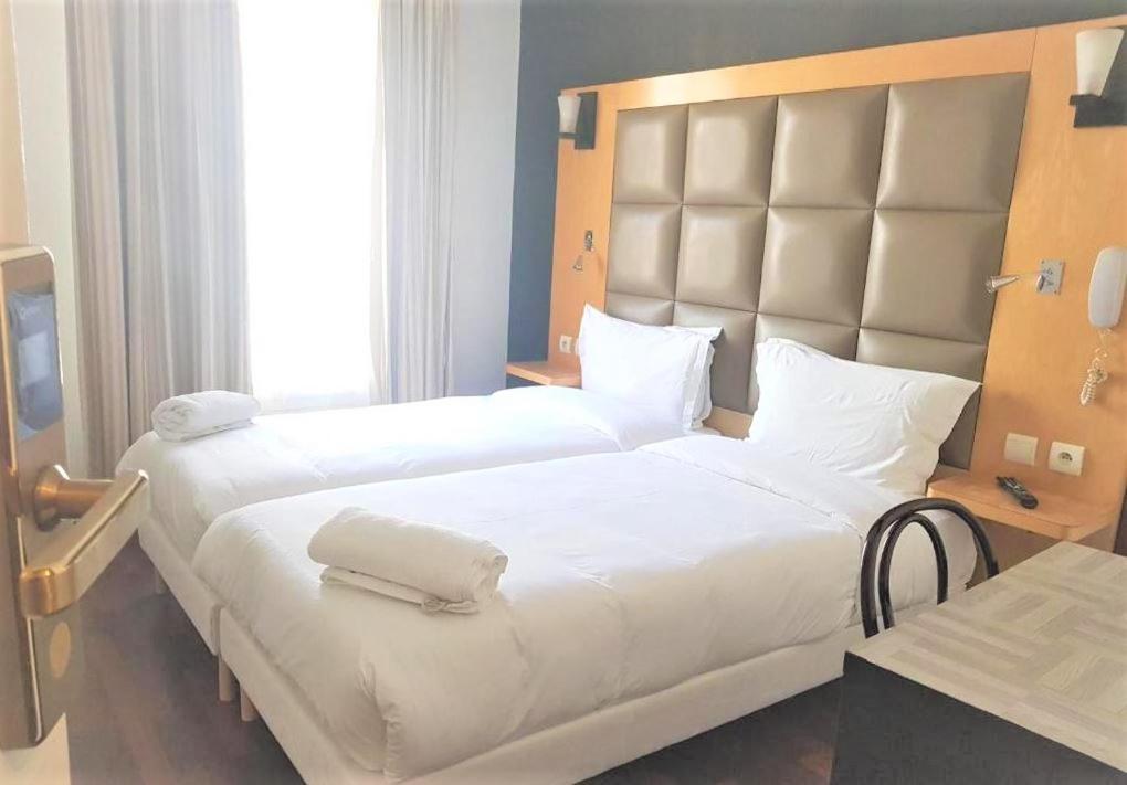 um quarto com 2 camas com lençóis brancos e uma grande cabeceira. em Hotel de France 18 em Paris