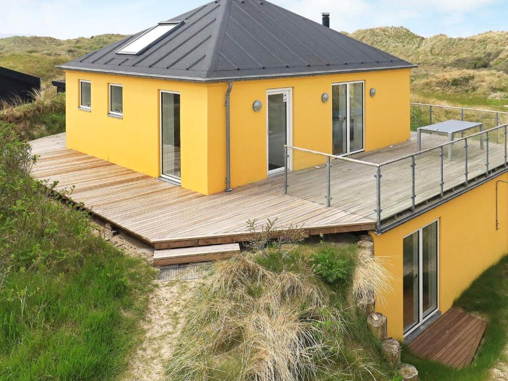 een geel huis met een houten terras op een heuvel bij 10 person holiday home in Brovst in Tranum Strand