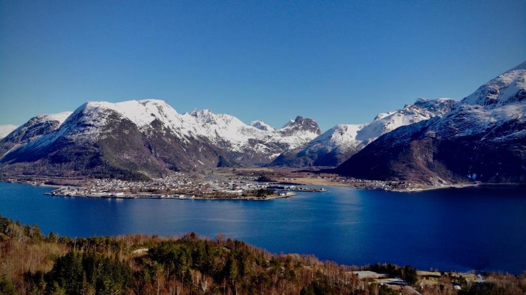 a town in the middle of a lake with snow covered mountains at Åndalsnes Sentrum 1-roms Apartment in Åndalsnes