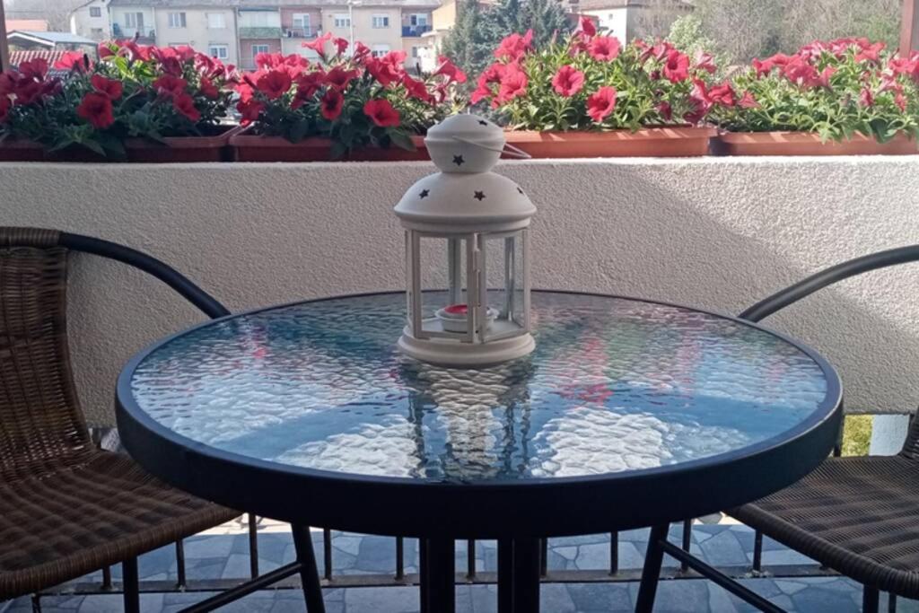 a glass table with a lantern on a balcony with flowers at Apartment Rajic in Golubac