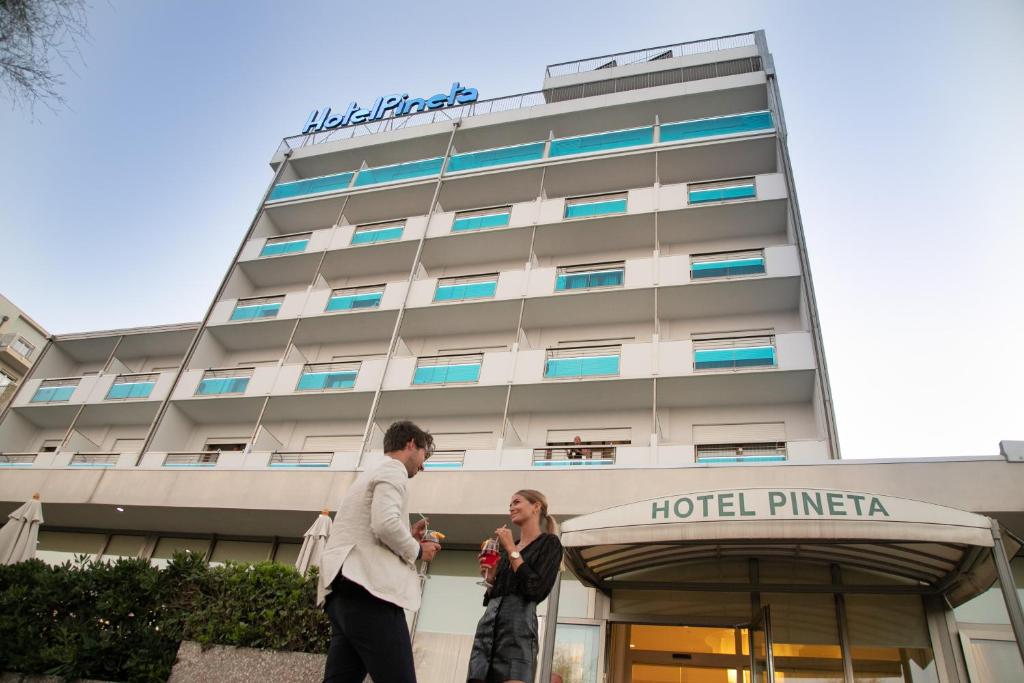 un hombre y una mujer caminando delante de un hotel en Hotel Pineta en Sottomarina