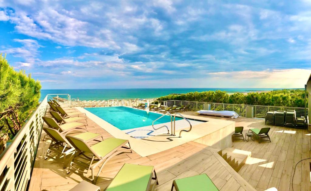 a balcony with a swimming pool and chairs and the ocean at Park Hotel Pineta & Dependance Suite in Eraclea Mare