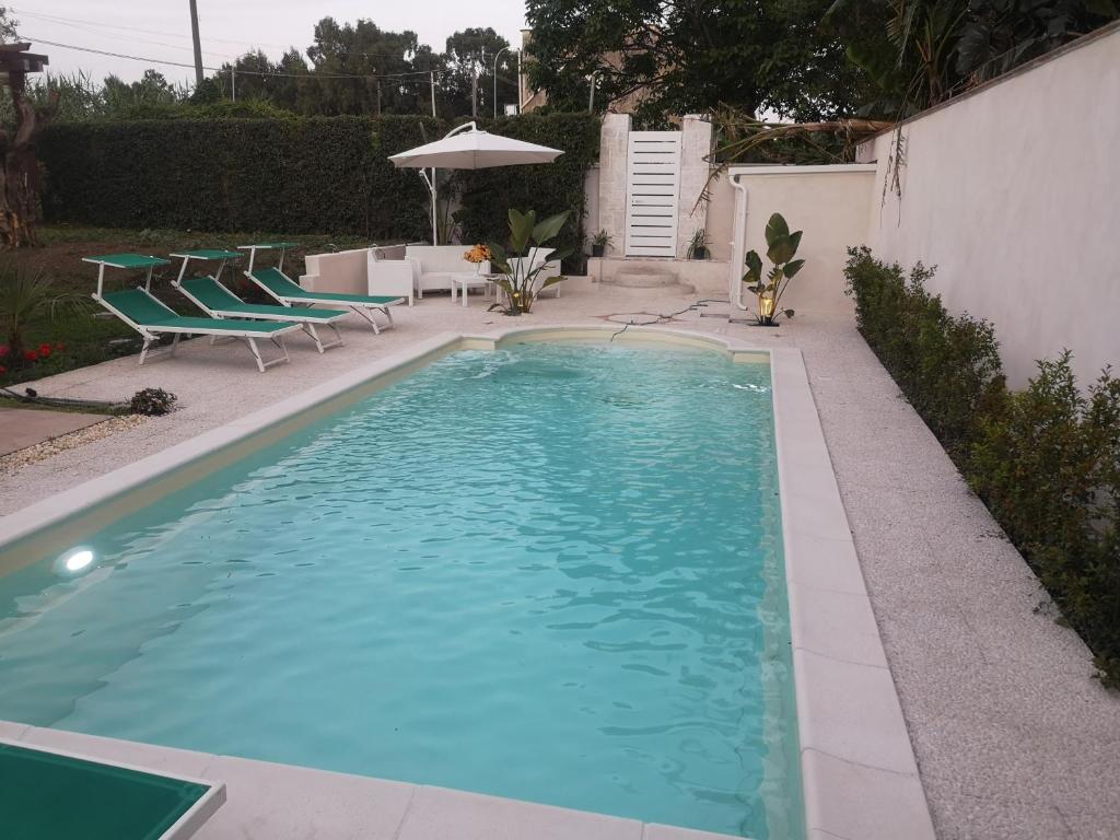 a swimming pool with chairs and a table and an umbrella at Bivano Villa Grazia in Fondachello