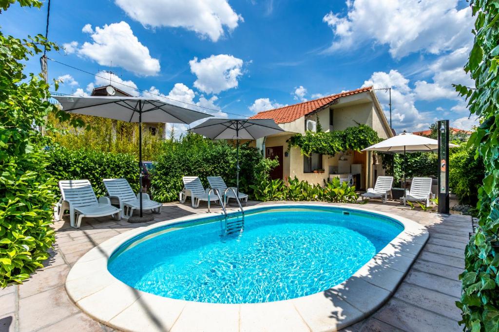a pool with chairs and umbrellas next to a house at Regina Apartments in Brodarica