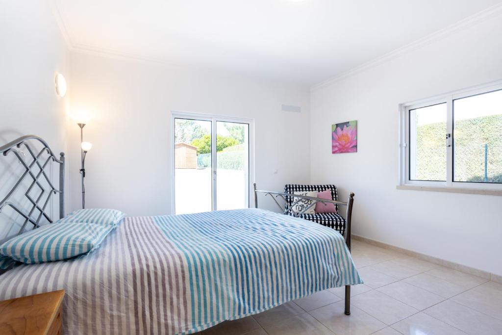 a white bedroom with a bed and a chair at Villa Flavia in Aljezur