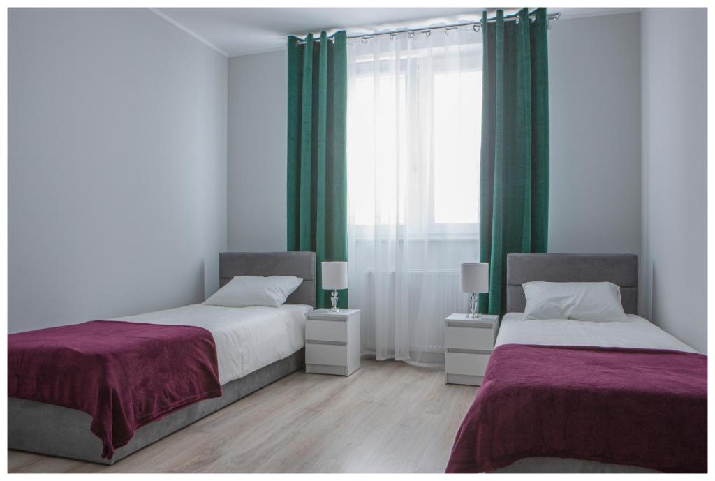 two beds in a bedroom with green curtains at Pokoje na wynajem in Gdańsk