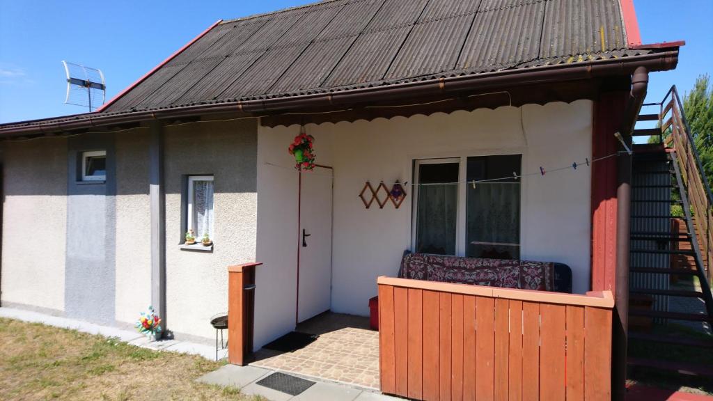 a small white house with a porch and a door at Dom Bursztynek - domek murowany in Junoszyno