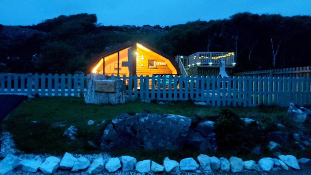 Una casita iluminada detrás de una valla por la noche en Achmelvich View self catering, en Lochinver