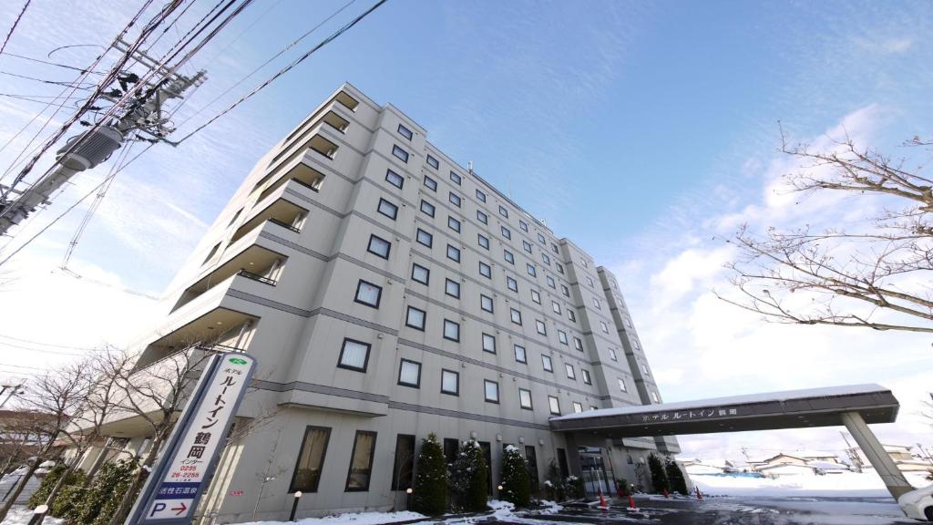 Un grand bâtiment blanc avec un panneau devant. dans l'établissement Hotel Route-Inn Tsuruoka Inter, à Tsuruoka