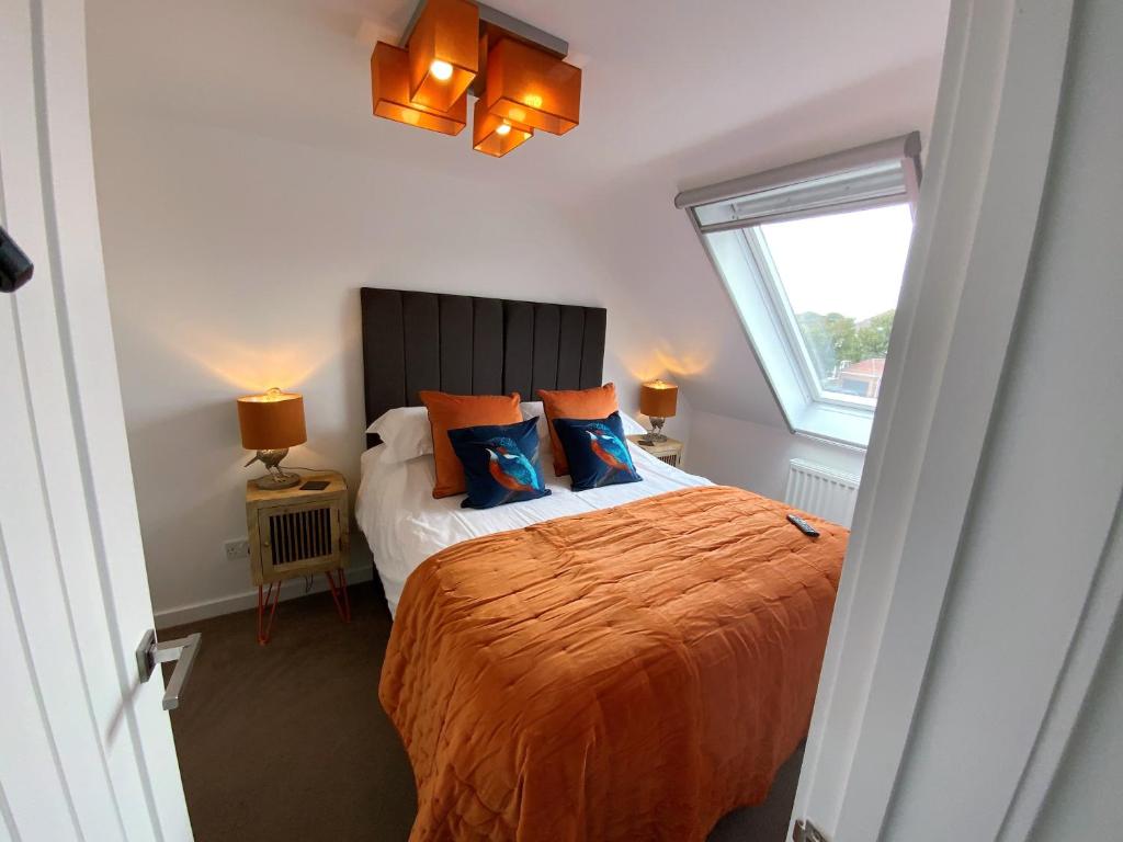 a bedroom with a bed with orange sheets and a window at THE HIDEAWAY - LUXURY SELF CATERING COASTAL APARTMENT with PRIVATE ENTRANCE & KEY BOX ENTRY JUST A FEW MINUTES WALK TO THE BEACH, SOLENT WAY WALK, SHOPS and many EATERIES & BARS - FREE OFF ROAD PARKING,FULL KITCHEN, LOUNGE,BEDROOM , BATHROOM & WI-FI in Lymington