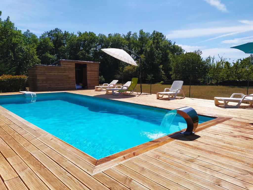una piscina en una terraza de madera con sillas y sombrilla en La maison d'iréne, en Soturac