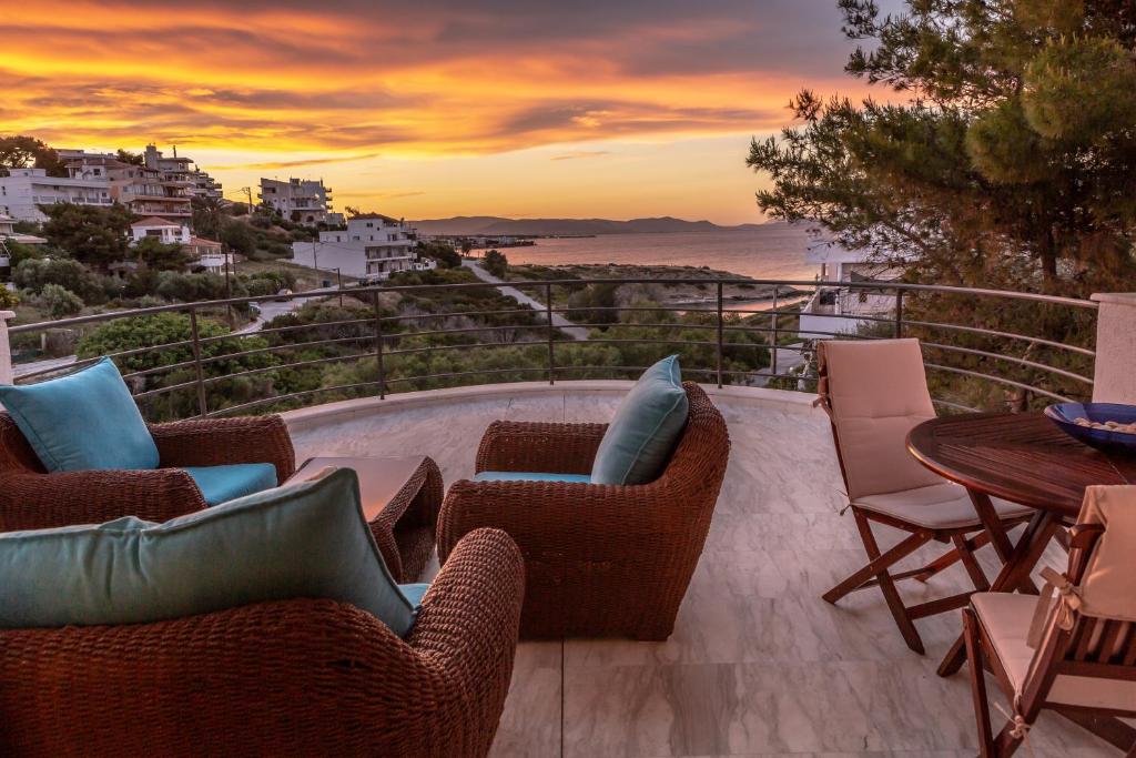 einen Balkon mit Stühlen, einem Tisch und einem Sonnenuntergang in der Unterkunft BIG BLUE in Rafina