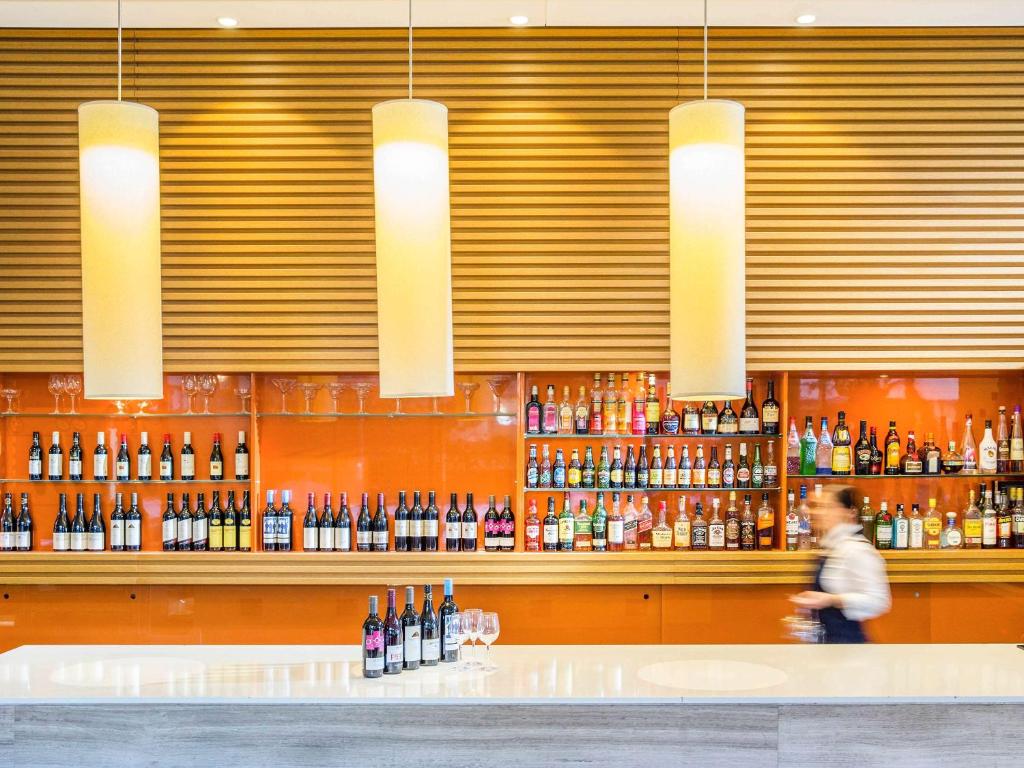 a man walking past a bar with bottles of wine at Novotel Newcastle Beach in Newcastle